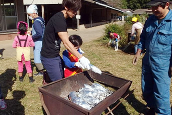 たき火に準備した焼き芋を投入する様子の写真