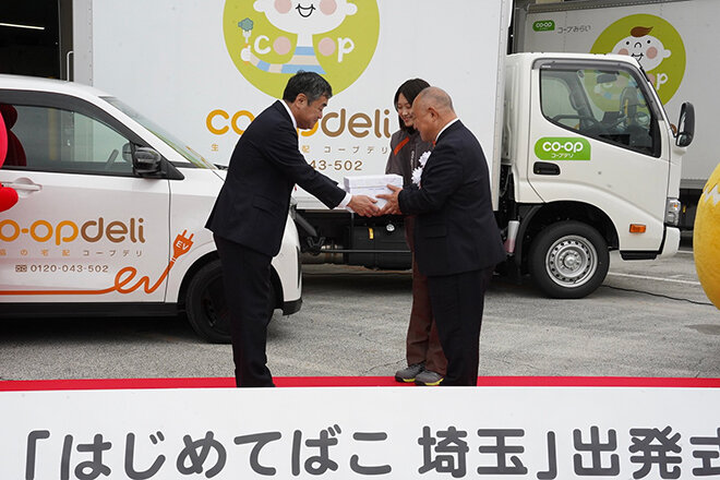 川原社長よりコープみらいの熊﨑理事長、職員の山田さんに箱を手渡す様子